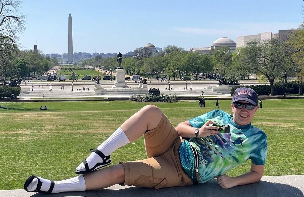 Elaine Honold as DC Dad, lounging in socks and sandals on the National Mall with the Washington Monument behind her